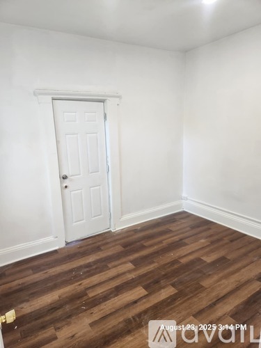 A room with a white door and wooden flooring.
