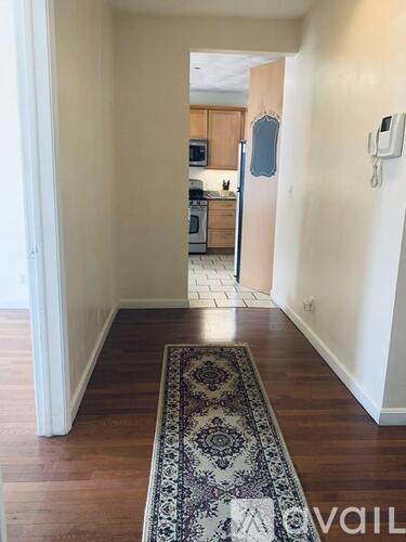 A hallway with a rug on the floor leading to a kitchen.