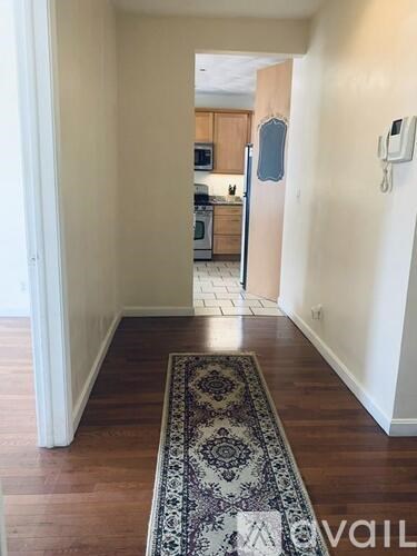 A hallway with a rug on the floor leading to a kitchen.