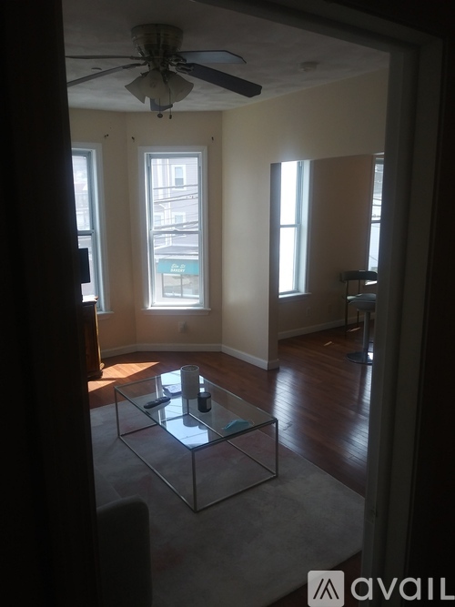 A living room with a glass coffee table and a ceiling fan.