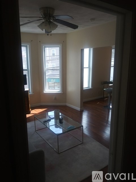 A living room with a glass coffee table and a ceiling fan.