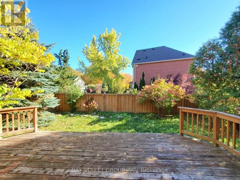 A wooden deck leads to a house with a red roof and a fence.