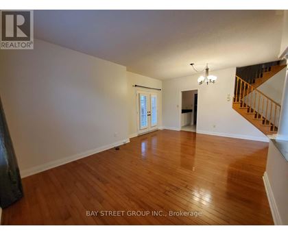 A spacious room with wooden floors and a staircase on the right side.