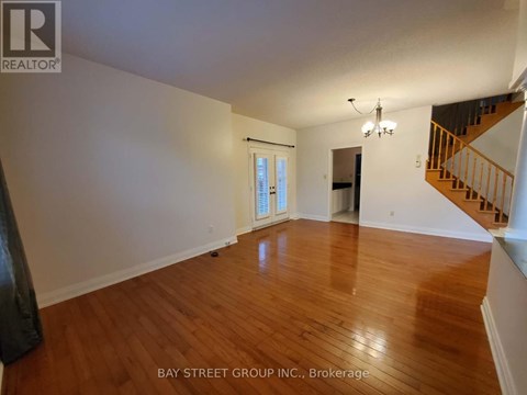 A spacious room with wooden floors and a staircase on the right side.