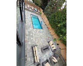 A small pool surrounded by a stone patio and wooden fence.
