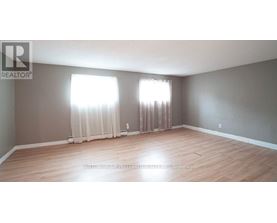 A room with wooden flooring and two windows with curtains.