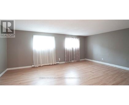 A room with wooden flooring and two windows with curtains.