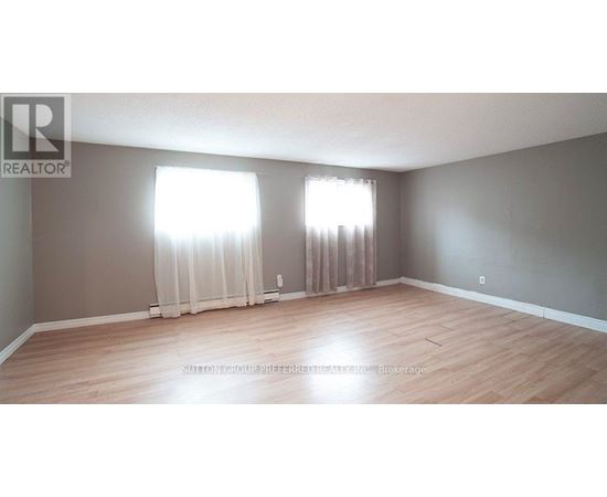 A room with wooden flooring and two windows with curtains.