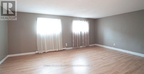 A room with wooden flooring and two windows with curtains.
