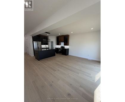 A spacious room with wooden flooring and a kitchen area in the background.