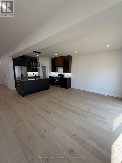 A spacious room with wooden flooring and a kitchen area in the background.