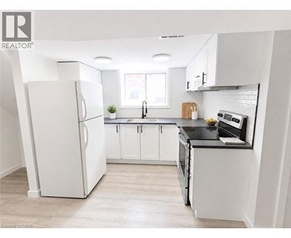 A white refrigerator stands in a kitchen with white cabinets and a black countertop.