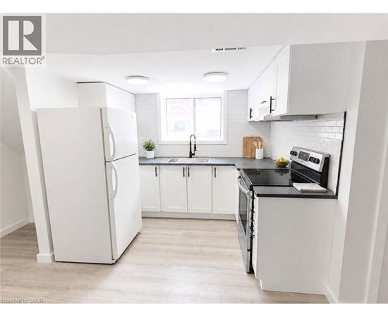 A white refrigerator stands in a kitchen with white cabinets and a black countertop.
