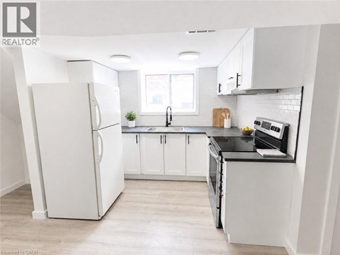 A white refrigerator stands in a kitchen with white cabinets and a black countertop.