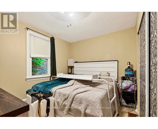 A bedroom with a bed, nightstand, and a window with a view of a garden outside.