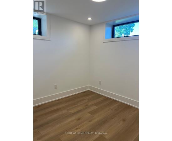 A room with wooden flooring and two windows.