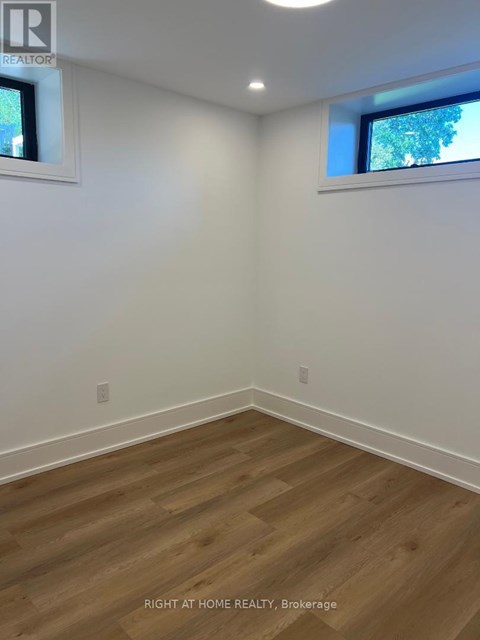A room with wooden flooring and two windows.