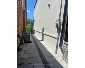 A sidewalk runs between a brick building and a concrete building.