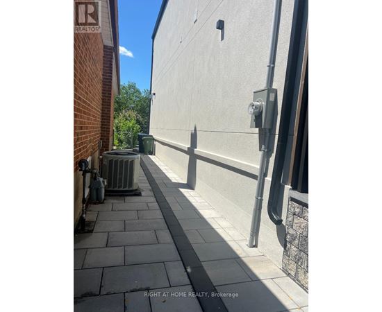 A sidewalk runs between a brick building and a concrete building.