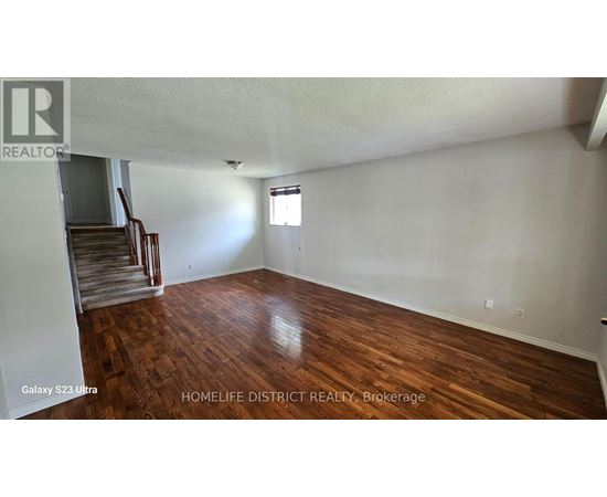 A room with wooden flooring and a staircase in the background.