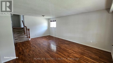 A room with wooden flooring and a staircase in the background.