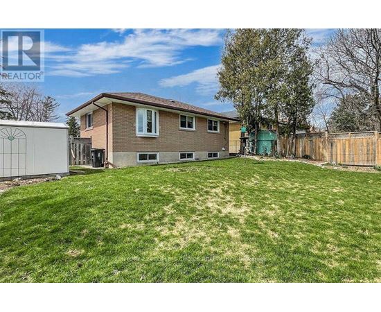 A house with a brown roof and a green door is surrounded by a fence and has a yard with a mix of green and brown grass.