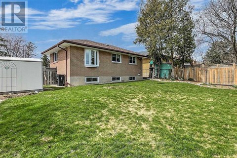 A house with a brown roof and a green door is surrounded by a fence and has a yard with a mix of green and brown grass.