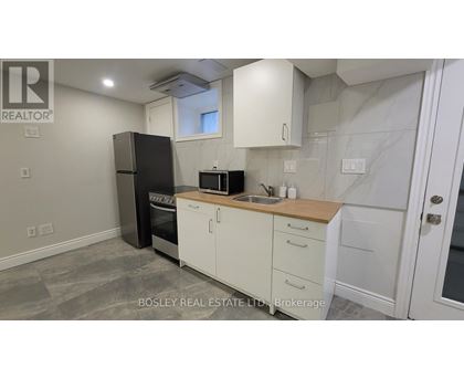 A kitchen with a black fridge, white cabinets, and a wooden countertop.