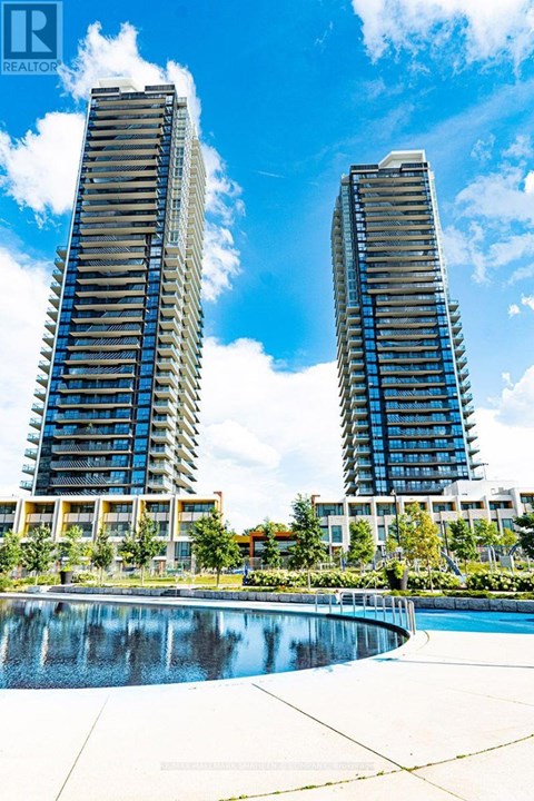 Two tall buildings with balconies are reflected in a pool.