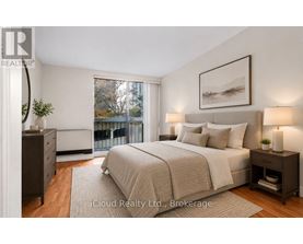 A bedroom with a large bed, a nightstand, and a window overlooking a balcony.