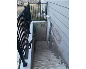 A stairway with a black railing leading to a concrete area.