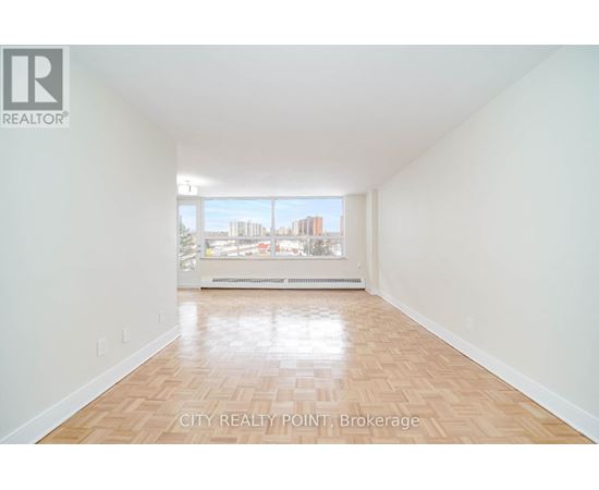A large empty room with wooden floors and a view of the city through the window.