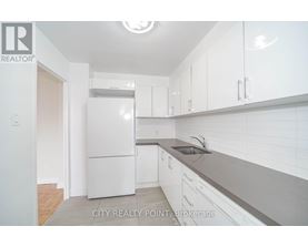 A white refrigerator is in a kitchen with white cabinets.