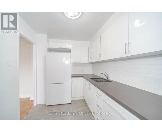 A white refrigerator is in a kitchen with white cabinets.
