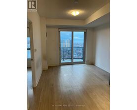 A spacious room with wooden flooring and a view of the city through large windows.