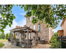 A gazebo is situated in a backyard with a patio and a brick house.