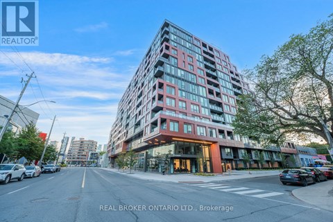 A modern multi-story building with a red and pink facade is situated on a street with cars parked on the side.