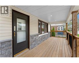 A wooden deck leads to a house with a stone wall and a glass door.
