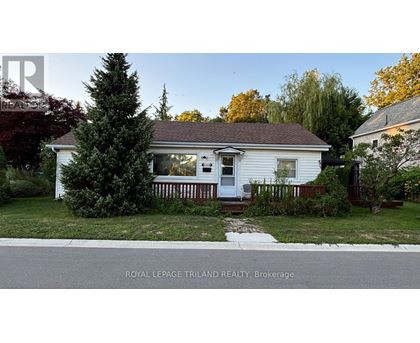 A white house with a porch and a tree in front of it.