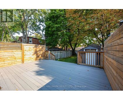 A wooden deck leads to a backyard with a fence and trees.