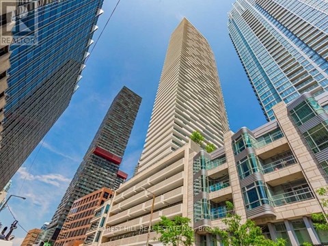 A tall building with a green plant on the side is in the foreground of a cityscape.