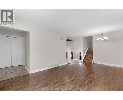 A spacious room with wooden floors and a staircase leading to another level.