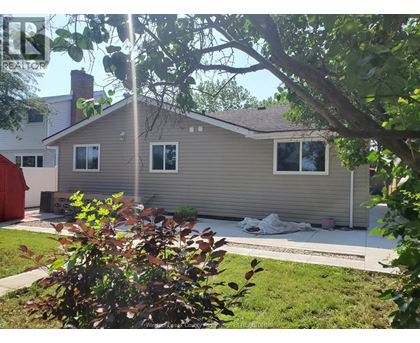 A house with a grey siding and a brown roof is surrounded by greenery.