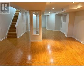 A spacious room with wooden flooring and a staircase leading to another level.