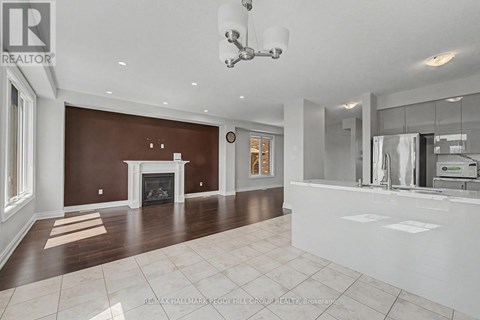 A large, empty living room with a fireplace and a kitchen area in the background.