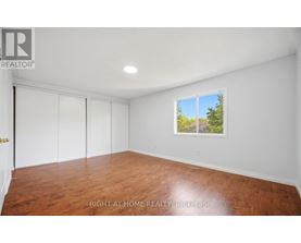 A room with wooden flooring and a window showing a view of trees.