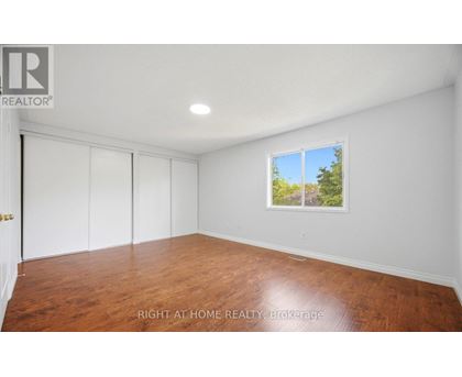 A room with wooden flooring and a window showing a view of trees.