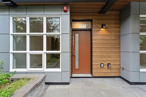 A modern house with a brown door and a red fire alarm on the wall.