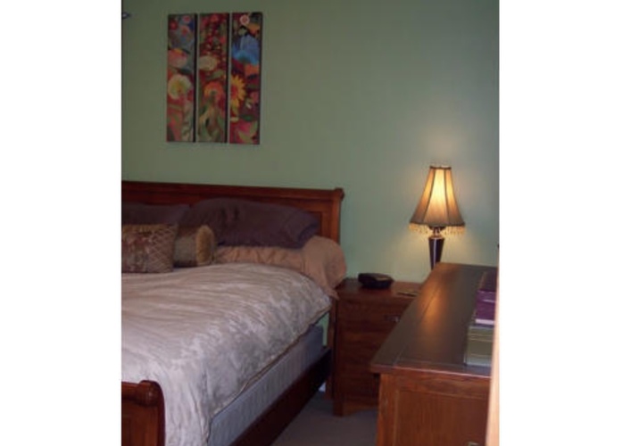 A bedroom with a bed, nightstand, lamp, and a painting on the wall.
