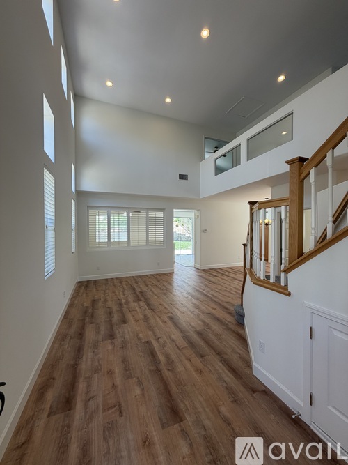 A spacious room with wooden floors and a staircase with white railings.